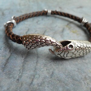 May include: A brown leather bracelet with a silver snake head clasp. The snake head is detailed with scales and has a small eye.