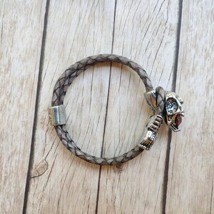 May include: A braided brown leather bracelet with a silver skull charm.