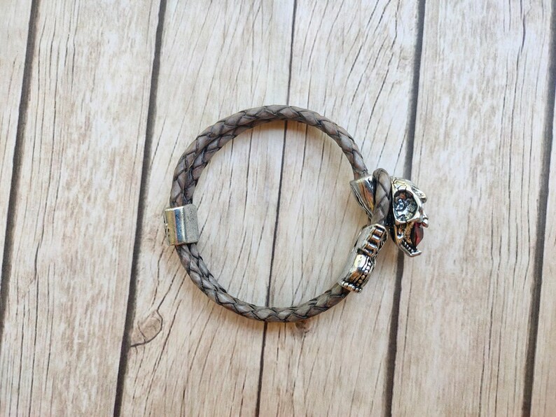 May include: A braided brown leather bracelet with a silver skull charm.