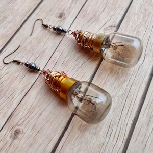 May include: A pair of dangle earrings featuring small light bulbs wrapped in copper wire and accented with black beads.