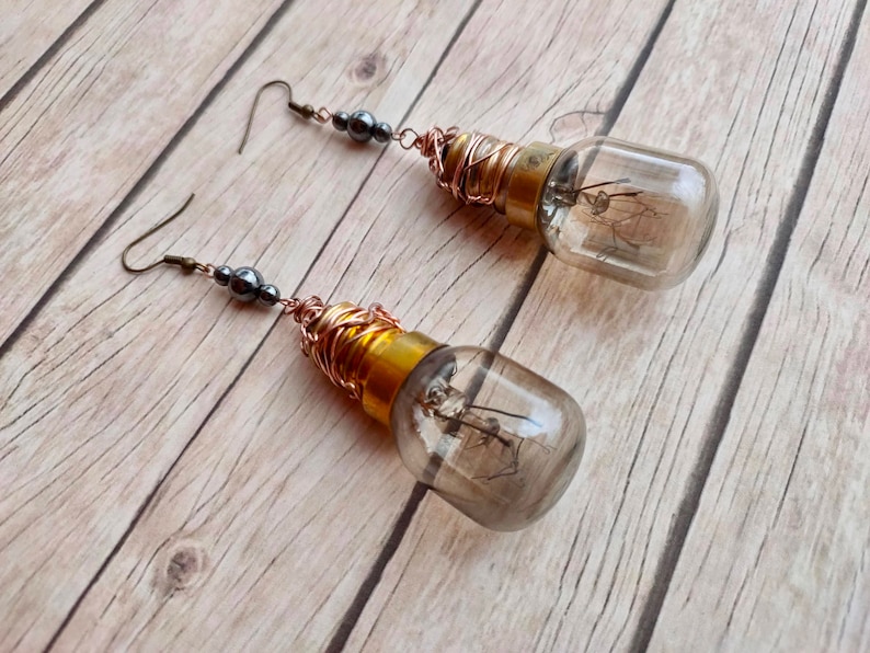 May include: A pair of dangle earrings featuring small light bulbs wrapped in copper wire and accented with black beads.