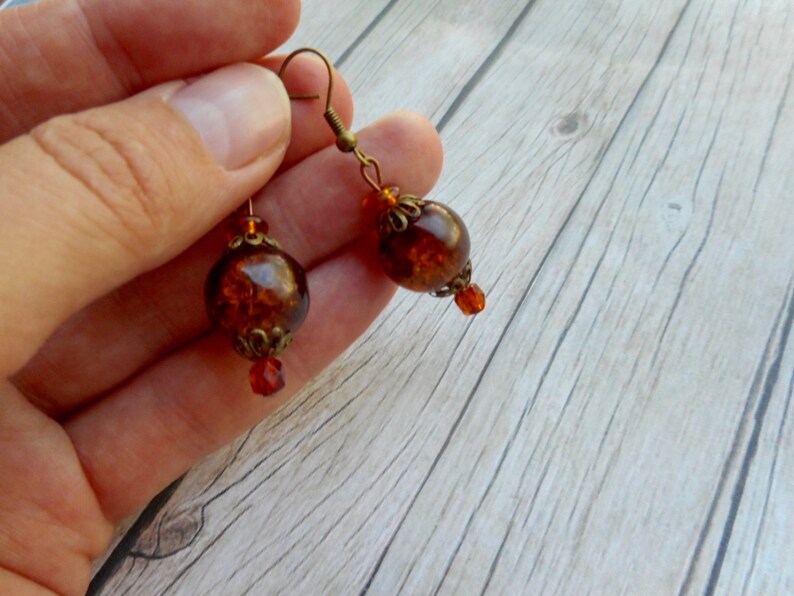 May include: A pair of amber glass earrings with bronze-colored metal accents and a small crystal bead hanging from each earring.