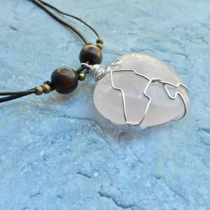 May include: A pink rose quartz heart pendant wrapped in silver wire, hanging from a brown leather cord with wooden beads.