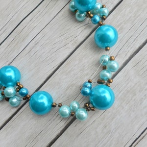 Peut inclure: Un collier de perles turquoise et bleu avec des perles brunes. Le collier est fait de perles grandes et petites.