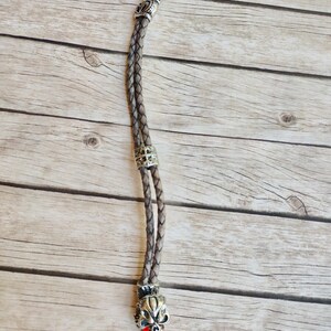 May include: A brown leather cord with a silver skull charm. The skull has a red gem for the tongue.
