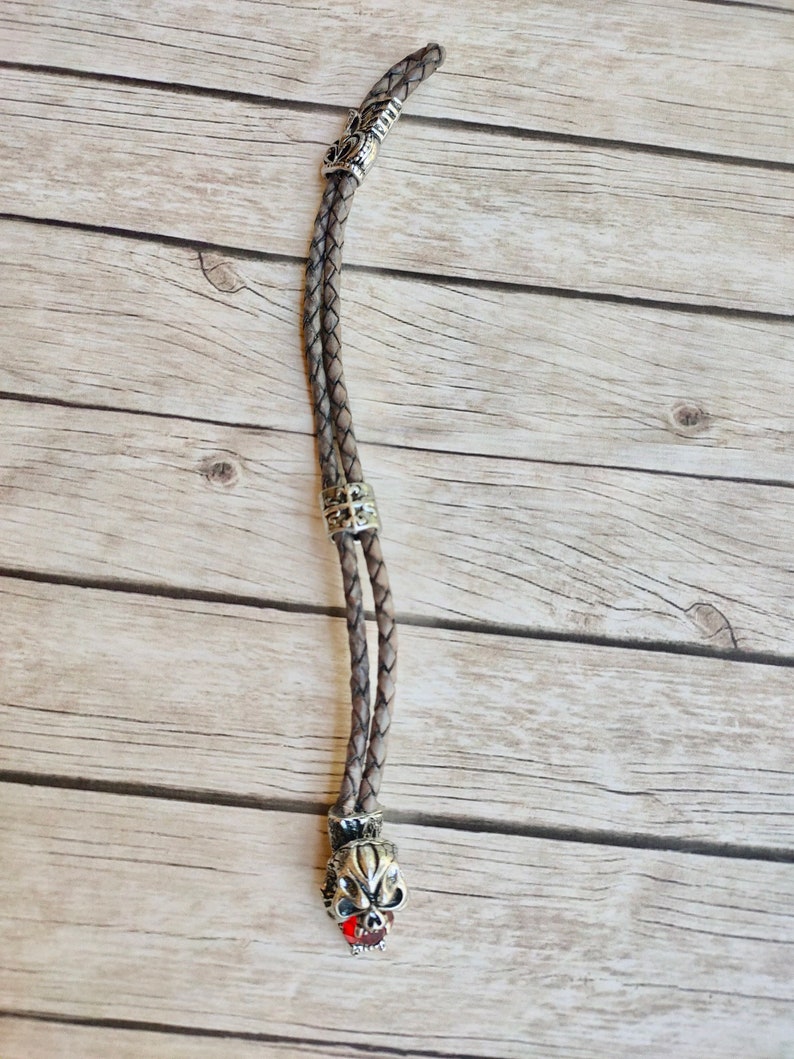 May include: A brown leather cord with a silver skull charm. The skull has a red gem for the tongue.