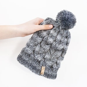 Mixed greys hand knitted cable pom pom hat. Women&#39;s thick chunky bobble beanie. Black/Grey mix, variegated yarn, textured winter accessory.