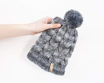 Mixed greys hand knitted cable pom pom hat. Women's thick chunky bobble beanie. Black/Grey mix, variegated yarn, textured winter accessory.