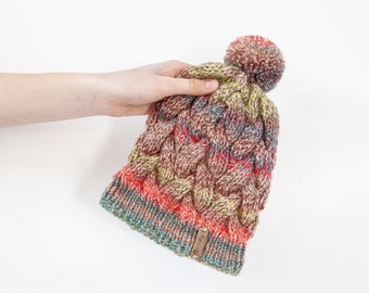 Colourful hand knitted cable pom pom hat. Women's thick chunky bobble beanie. Red mix, variegated yarn, textured winter accessory.