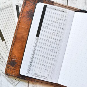 Op de afbeelding: Een bruin lederen dagboek met een zwart-witte dagelijkse tracker-inzet. De tracker heeft een raster met de nummers 17 tot en met 31. Het dagboek heeft een gestippelde pagina en de tekst "The Good Life Planner Co."