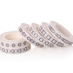 Op de afbeelding: Vijf rollen witte washi tape met zwarte patronen. De patronen omvatten harten, bomen, cirkels, vierkanten en strikken.