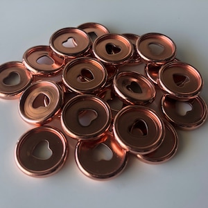 Puede incluir: Un montón de clips de encuadernación de metal de color oro rosa con un recorte en forma de corazón en el centro de cada clip.