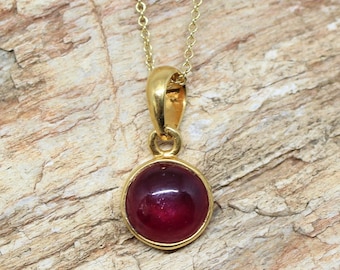 Könnte beinhalten: Eine goldene Kettenkette mit einem Anhänger mit einem runden, cabochon geschliffenen Rubin-Edelstein.