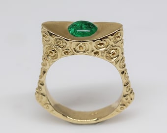 May include: A gold ring with a green gemstone set in a textured band.
