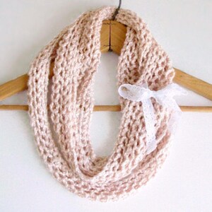 Peut inclure: Une écharpe en crochet infinie rose pâle avec un nœud en dentelle blanche.