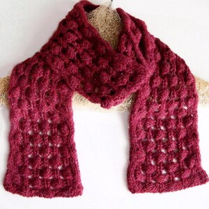 May include: A burgundy crocheted scarf with a lacy pattern. The scarf is folded in half and draped over a hanger.