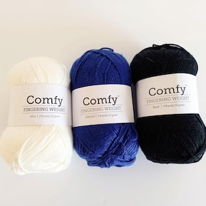 Op de afbeelding: Drie bollen Comfy Fingering Weight garen in wit, hemelsblauw en zwart. Elke bol is voorzien van de merknaam en de garendikte. De witte bol bevat 200 meter/50 gram, de blauwe bol 200 meter/50 gram en de zwarte bol 200 meter/30 gram.