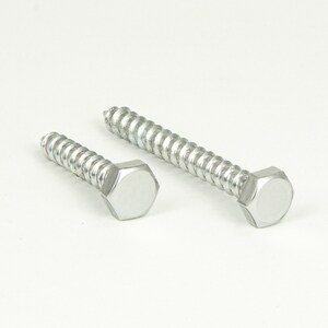 Puede incluir: Dos tornillos de color plateado con cabezas hexagonales. Los tornillos tienen un vástago roscado y están diseñados para su uso en madera u otros materiales.