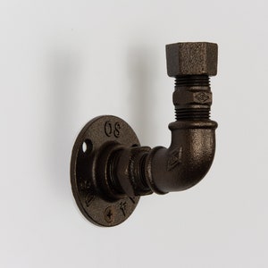 Könnte beinhalten: Ein brauner Metall-Rohrhaken mit einer Flansch. Der Flansch hat die Nummer "80" aufgedruckt. Der Haken hat die Form eines 90-Grad-Bogens.