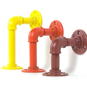 May include: Three metal pipe fittings in yellow, orange, and brown. Each fitting has a 90-degree bend and a flange with a number stamped on it.