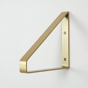 Könnte beinhalten: Ein goldfarbenes Metallregal in Dreiecksform. Das Regal hat zwei Löcher zur Montage.