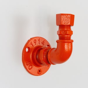 Könnte beinhalten: Orangefarbenes Metallrohrfitting mit Flansch und 90-Grad-Bogen. Das Fitting trägt die Zahlen "1914" und "80".