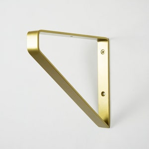 Könnte beinhalten: Goldenes Metall-Regalhalterung mit dreieckiger Form und zwei Schraubenlöchern.