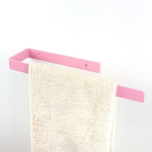 Può includere: Un portasciugamani in metallo rosa dal design rettangolare, montato su una parete bianca. Un asciugamano color crema è appeso al portasciugamani. Design semplice e moderno.
