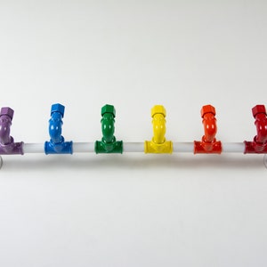 May include: A white metal pipe with six colourful hooks. The hooks are painted in the colours of the rainbow, starting with purple and ending with red.