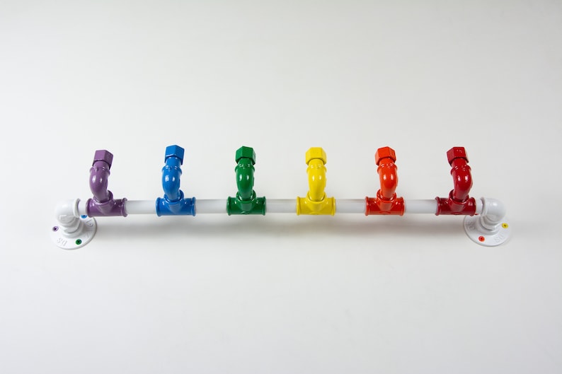 May include: A white metal pipe with six colourful hooks. The hooks are painted in the colours of the rainbow, starting with purple and ending with red.