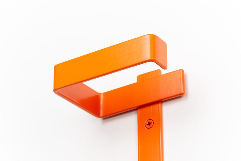 Op de afbeelding: Fel oranje metalen beugel met een rechthoekig ontwerp. De beugel is gemonteerd op een wit oppervlak en vastgezet met een schroef. Het ontwerp heeft een bovendeel en een verticale steun.