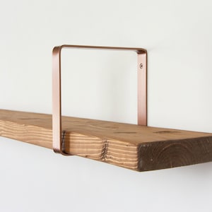 May include: A wooden shelf with copper metal brackets. The shelf is made of natural wood with a rustic finish. The brackets are a simple, modern design.