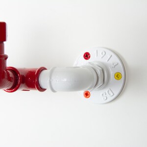 May include: A red and white pipe fitting with a white flange. The flange has the text "DS 1914" on it. The pipe fitting has a red elbow and a red cap with the text "5/2" on it.