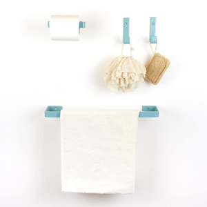 Könnte beinhalten: Ein Badezimmer-Set mit hellblauen Elementen: Handtuchhalter, Toilettenpapierhalter und zwei Haken. Ein weißes Handtuch hängt am Halter, und eine Rolle Toilettenpapier befindet sich im Halter. Zwei Badezimmer-Accessoires hängen an den Haken.
