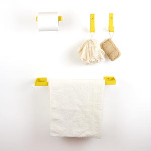 Può includere: Un set da bagno giallo brillante che include un portarotolo di carta igienica, due ganci e un portasciugamani. Sono visibili un asciugamano bianco e un rotolo di carta igienica. Una spugna vegetale beige e una spugna marrone sono appese ai ganci.