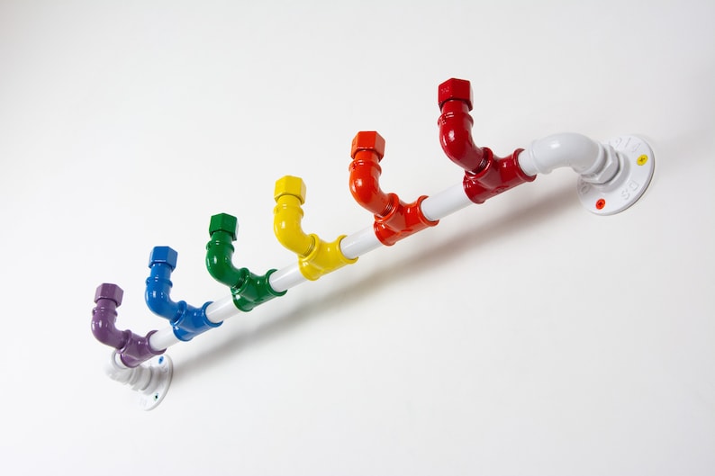 May include: A rainbow coloured pipe coat rack with a white pipe and a white wall mount. The rack has seven hooks, each a different colour of the rainbow.