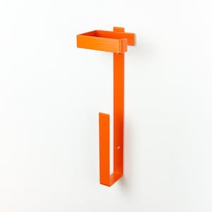 Op de afbeelding: Fel oranje aan de muur gemonteerde papieren handdoekhouder. De houder heeft een rechthoekig bovendeel, een lange verticale balk en een U-vormig onderste deel. Het ontwerp is eenvoudig en modern, met een strakke, minimalistische esthetiek.