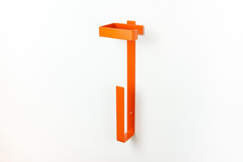 Op de afbeelding: Fel oranje aan de muur gemonteerde papieren handdoekhouder. De houder heeft een rechthoekig bovendeel, een lange verticale balk en een U-vormig onderste deel. Het ontwerp is eenvoudig en modern, met een strakke, minimalistische esthetiek.