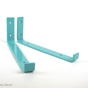 May include: Two light blue metal shelf brackets with rounded edges and two holes on each bracket. The brackets are angled and the ends are curved.