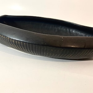 May include: A black ceramic planter with a ribbed texture. The planter is shaped like a boat and has a wide, shallow opening.