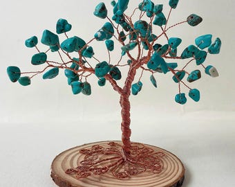 May include: A decorative tree sculpture featuring a twisted copper wire trunk and branches adorned with numerous small, irregular turquoise-colored stones. The base is a circular slice of natural wood with visible rings.