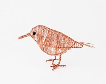 May include: A bird sculpture crafted from thin copper wire, featuring a rounded body, a pointed beak, and a single small black bead for an eye. The wire is wrapped in a dense, layered pattern to form the shape of the bird, standing on two wire feet.