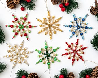 May include: Six handmade snowflake ornaments crafted from metallic gold tubes and various colored beads. The ornaments feature red and green, gold, blue, white, green, and red color schemes, each with a thin wire loop for hanging purposes.