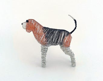 May include: A wire sculpture of a dog featuring a tri-color pattern. The head and back are crafted from copper-colored wire, while the legs are made of silver-colored wire. The dog has a black patch on its back, a black tail, and black eyes.