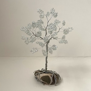 May include: A small, silver wire tree with clear glass beads for leaves. The tree is sitting on a brown and white stone base.