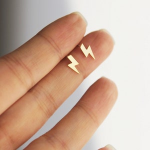May include: A pair of gold lightning bolt stud earrings. The earrings are small and delicate, and they are perfect for adding a touch of edgy style to any outfit.