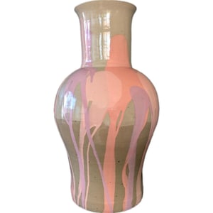 Op de afbeelding: Een keramische vaas met een brede basis en een smalle hals. De vaas is voornamelijk beige met roze en lavendelkleurige verfdruppels die langs de zijkanten naar beneden lopen. De bovenste rand is lichtbeige.