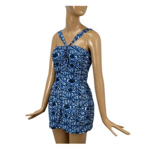 May include: A sleeveless romper featuring a blue and white geometric pattern with a halter neckline. The garment has a fitted bodice and a short hemline, showcasing a repeating design of diamonds, lines, and floral-like shapes across the fabric.