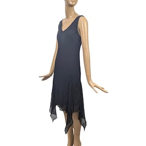 May include: A sleeveless, dark navy blue dress with a V-neckline and a handkerchief hem. The dress features delicate ruffle detailing along the bodice and hemline. The dress is displayed on a mannequin.