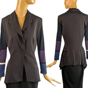 May include: A dark brown blazer with color-blocked sleeves. The sleeves feature sections of black, purple, blue, and white. The blazer has a notched collar, two front pockets, and three buttons. The back of the blazer has a peplum design.